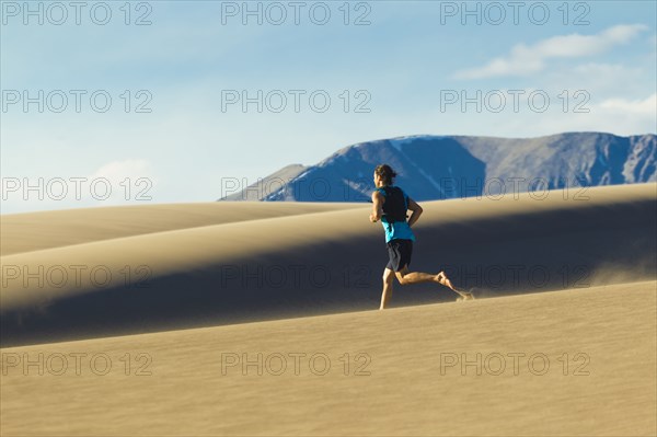 Hispanic man running on sand dune