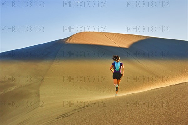 Hispanic woman running on sand dune