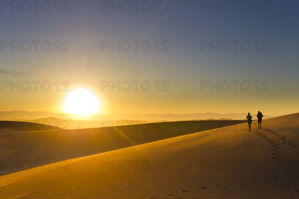 Hispanic couple walking on sand dune at sunset