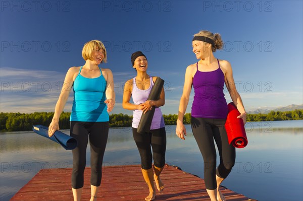 Women carrying yoga mats on lake pier