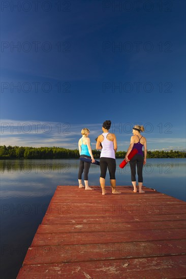 Women holding yoga mats on lake pier