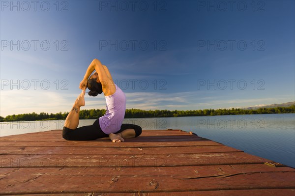 Korean woman practicing yoga on lake pier