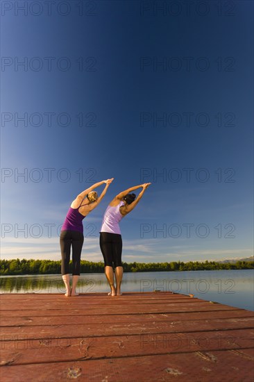 Woman practicing yoga on lake pier