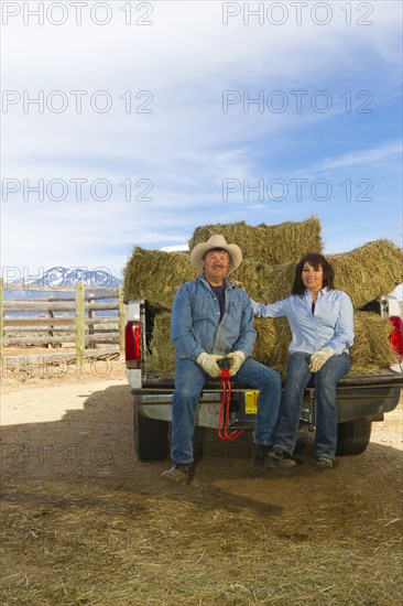 Hispanic couple sitting on back of truck full of hay