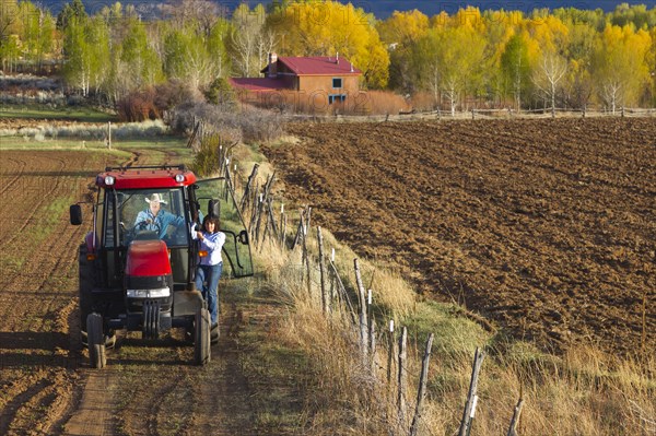 Hispanic couple driving tractor on farm