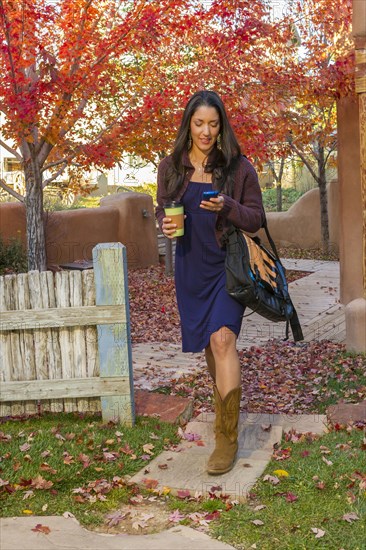 Hispanic woman carrying coffee and text messaging on cell phone