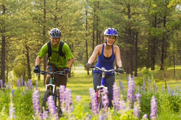 Couple riding mountain bikes in meadow