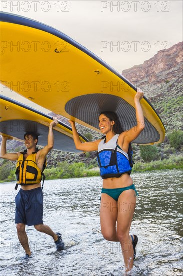 Hispanic couples carrying paddle boards in water