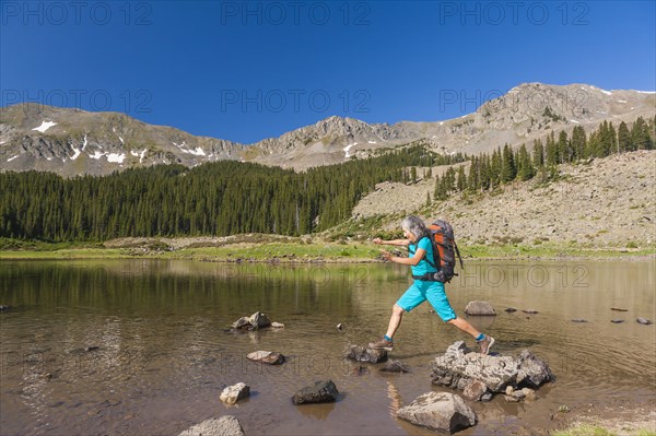 Hispanic hiker climbing on rocks in lake