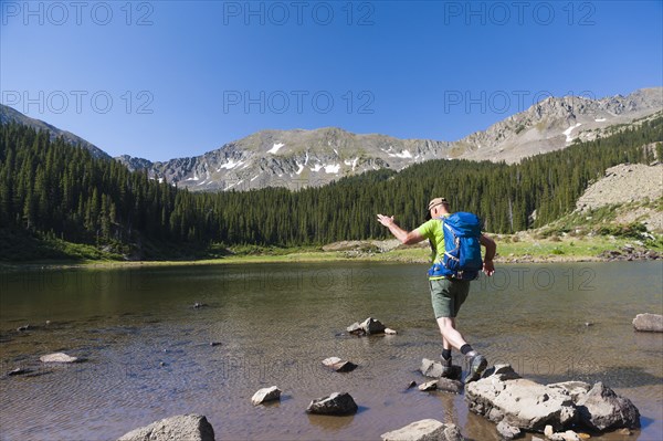 Caucasian hiker climbing on rocks in lake