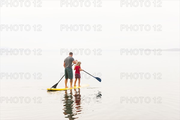 Caucasian father and daughter riding paddle board