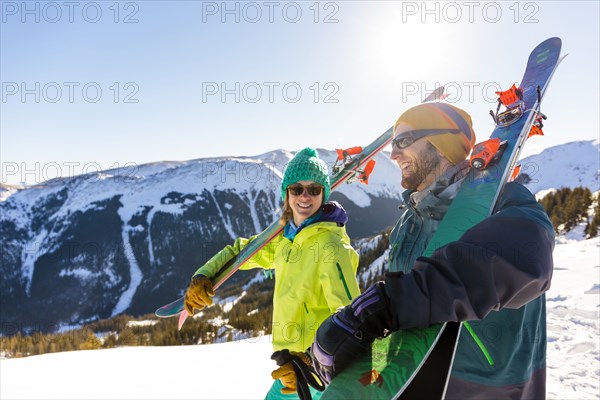 Couple carrying skis on snowy mountain