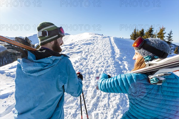 Couple carrying skis on snowy mountain