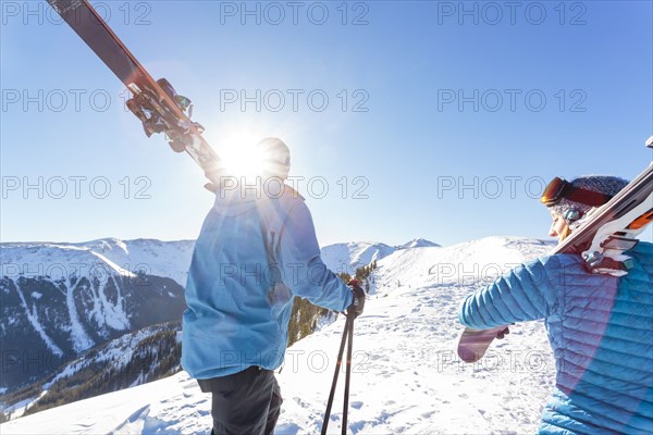 Couple carrying skis on snowy mountain