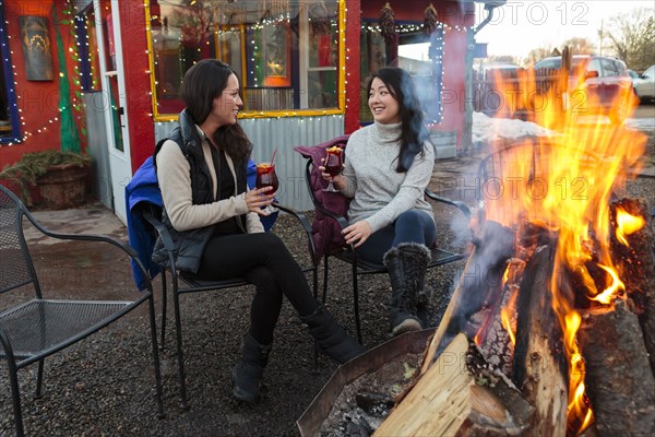 Women drinking cocktails outdoors at storefront campfire