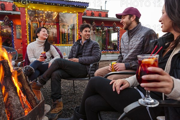 Couples drinking cocktails and beer outdoors at storefront campfire