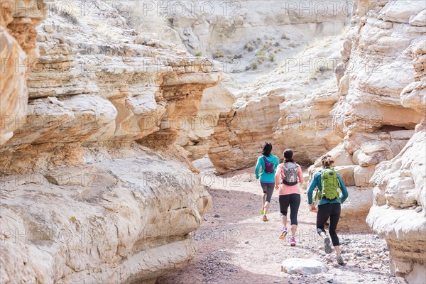 Women running in canyon wearing backpacks