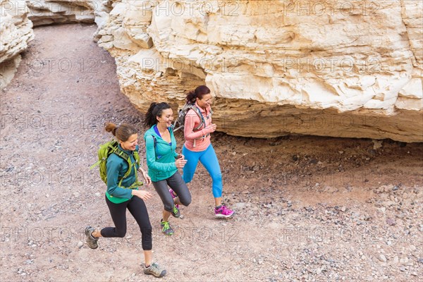 Women running in canyon wearing backpacks