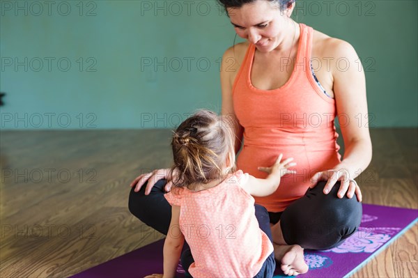 Mixed Race girl touching belly of expectant mother on exercise mat