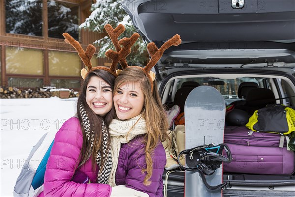 Women posing near car in winter wearing toy antlers