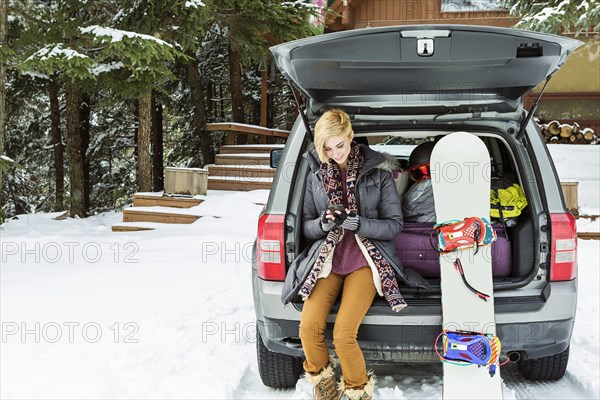 Caucasian woman at car texting on cell phone in winter