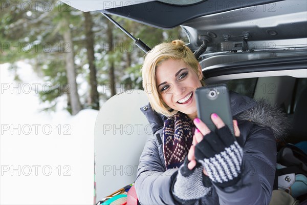 Caucasian woman at car posing for cell phone selfie in winter