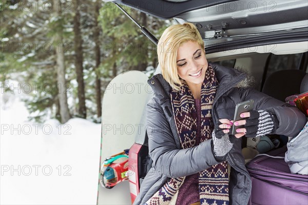 Caucasian woman at car texting on cell phone in winter