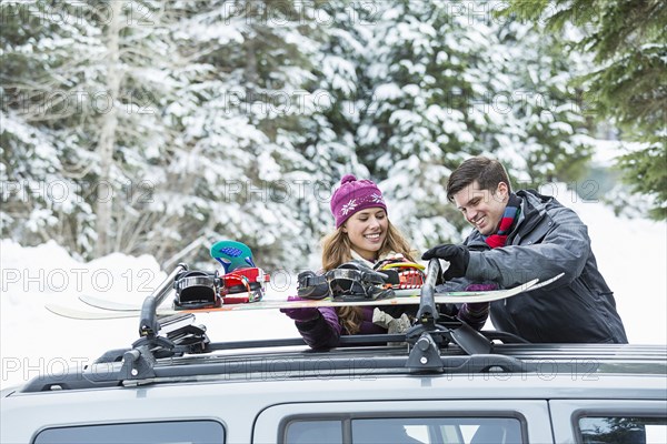 Caucasian couple checking snowboards in car roof rack