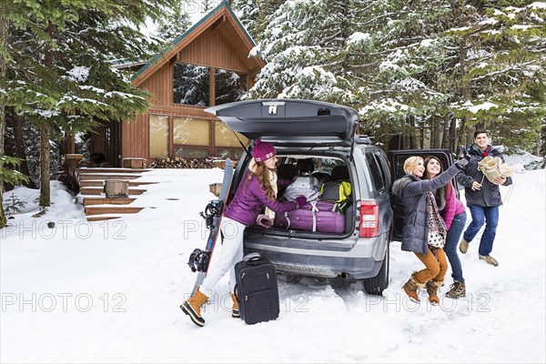 Friends posing for cell phone selfie near car in winter