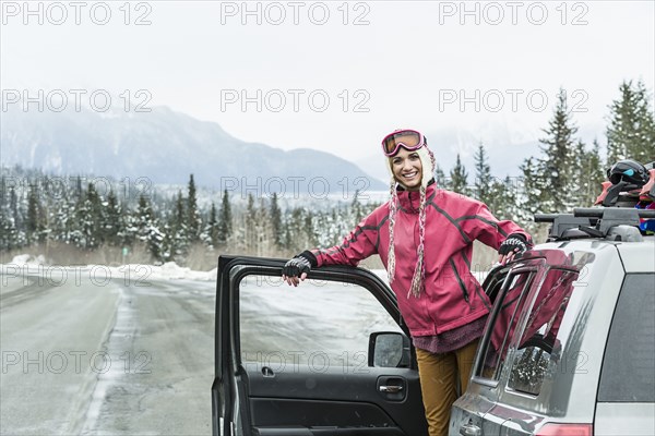 Smiling Caucasian woman standing in car in winter