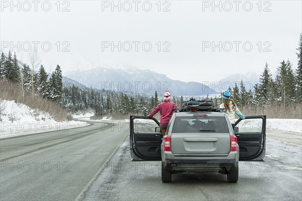 Caucasian women standing in car in winter admiring scenic view