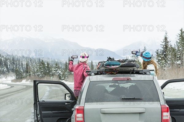 Caucasian women standing in car in winter photographing scenic view