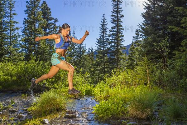 Hispanic woman jumping over stream