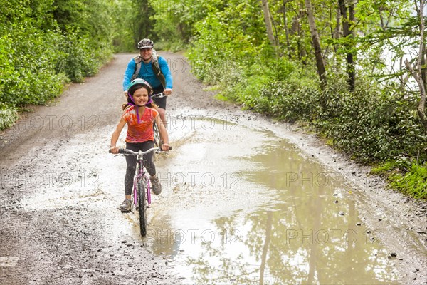 Father and daughter riding bicycles through puddle