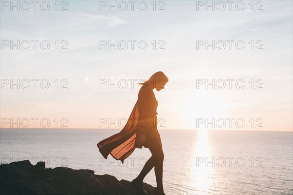 Silhouette of Caucasian woman walking on rocks at ocean