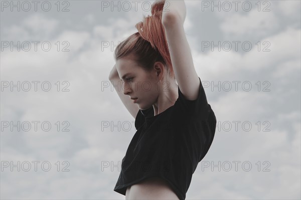 Caucasian woman arranging hair against clouds