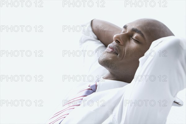 Mixed race businessman with hands behind head and eyes closed