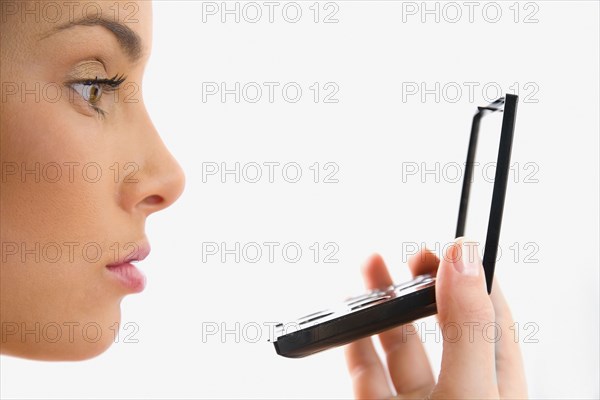 Mixed race woman looking at reflection in compact mirror