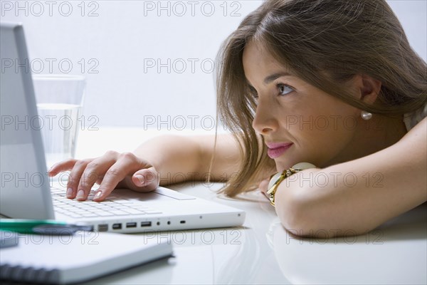 Mixed race businesswoman laying on desk using laptop