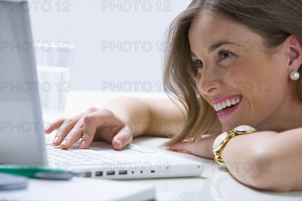 Mixed race businesswoman laying on desk using laptop