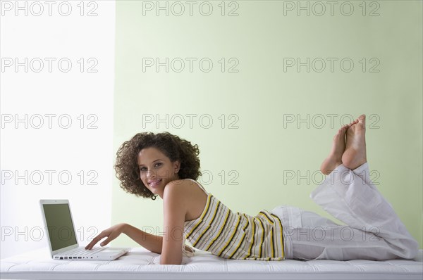 Mixed race woman laying on sofa using laptop