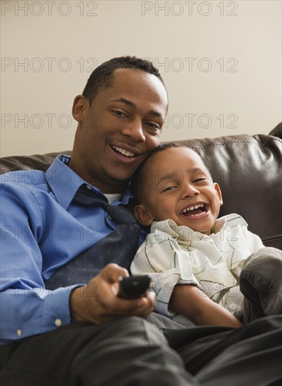 Father and son sitting on sofa watching television