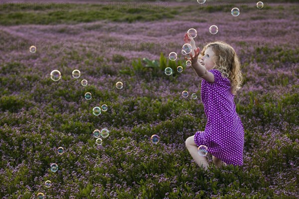 Caucasian girls chasing bubbles in field of flowers