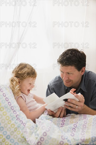 Caucasian father reading book to daughter in bed