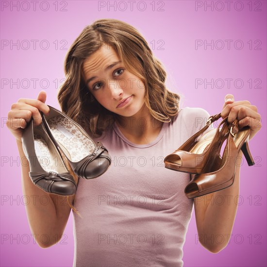 Uncertain Caucasian teenager holding shoes