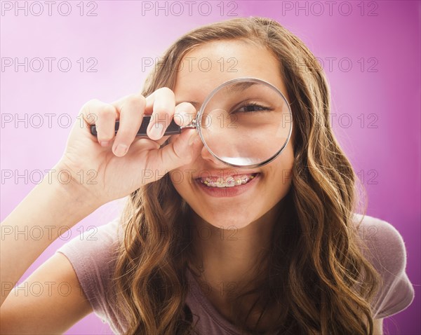 Caucasian teenager peering through magnifying glass