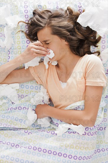 Caucasian teenager laying in bed blowing her nose