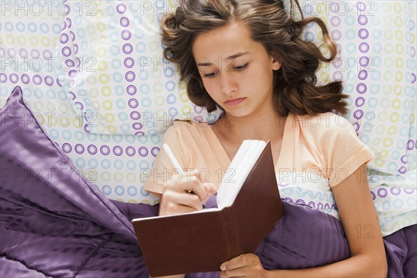 Caucasian teenager laying in bed writing in journal