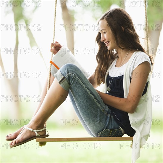 Caucasian girl reading book on swing