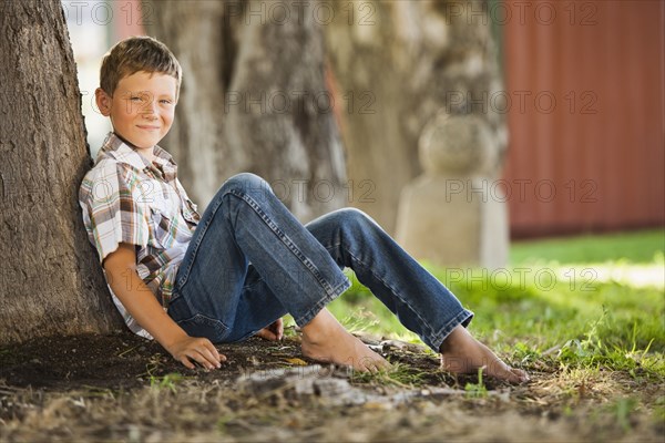 Caucasian boy leaning against tree trunk